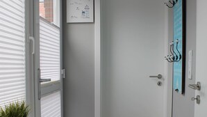 A narrow hallway with a white door, a small white bench, and a wall-mounted light fixture.