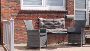 A patio with two wicker chairs, a cushioned bench, and a small round table.