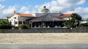 A beachfront property with a thatched-roof structure, a stone wall, and a clear view of the ocean. - Casa Cardonal - El Cardonal, BCS Mexico (El Cardonal)