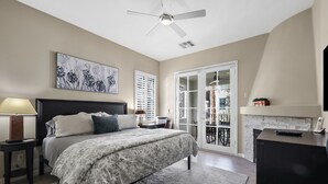 A bedroom with a bed, a nightstand, a lamp, a ceiling fan, a fireplace, and a sliding glass door to a balcony. - Have Fun and Relax at Luxury Legacy Villa. Family Friendly or Great for Couples! (La Quinta)