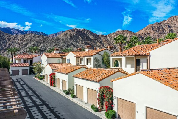A residential street with houses featuring red-tiled roofs, white walls, and garage doors.