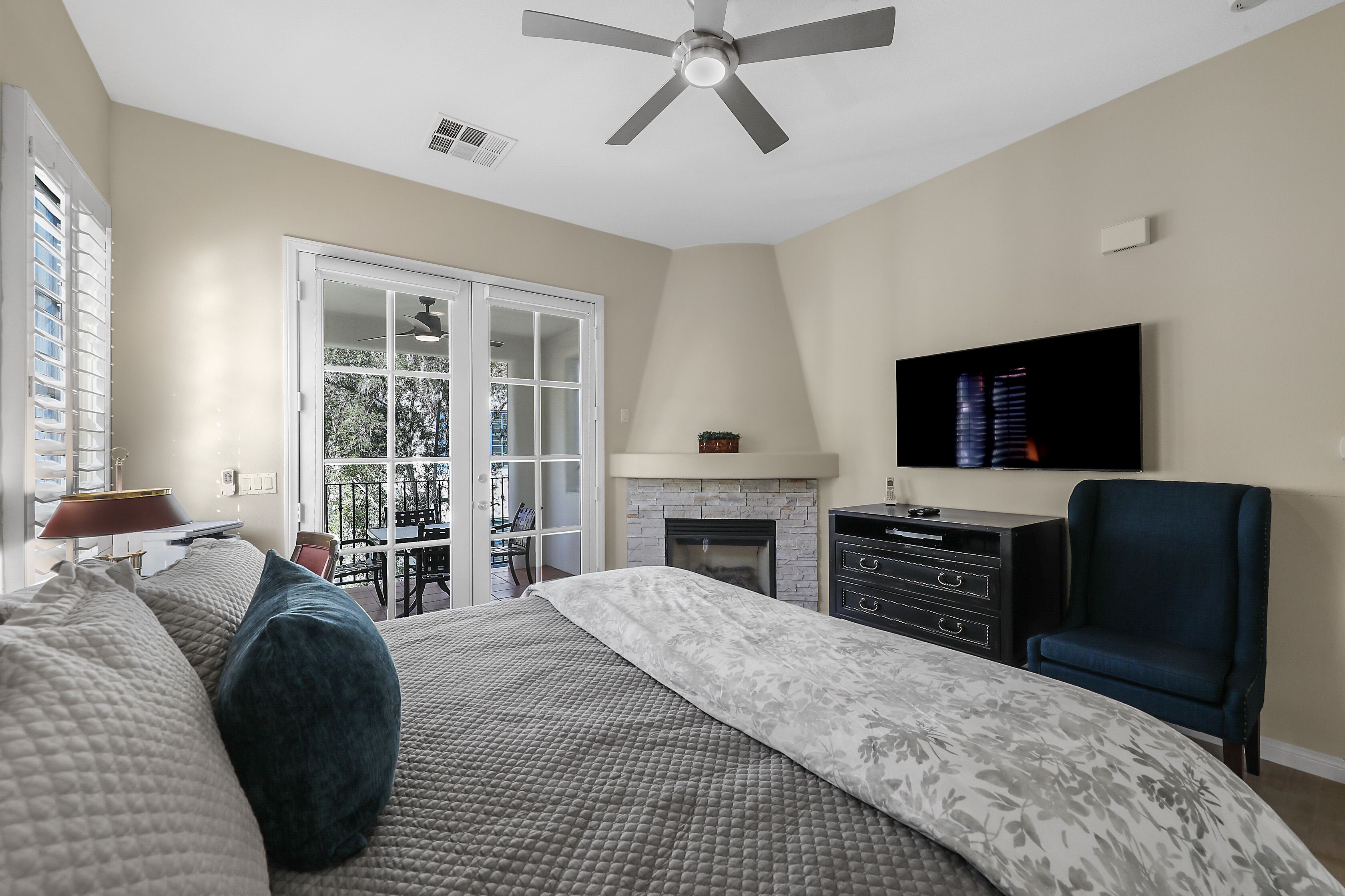 A bedroom with a bed, a TV, a chair, a fireplace, and a balcony.