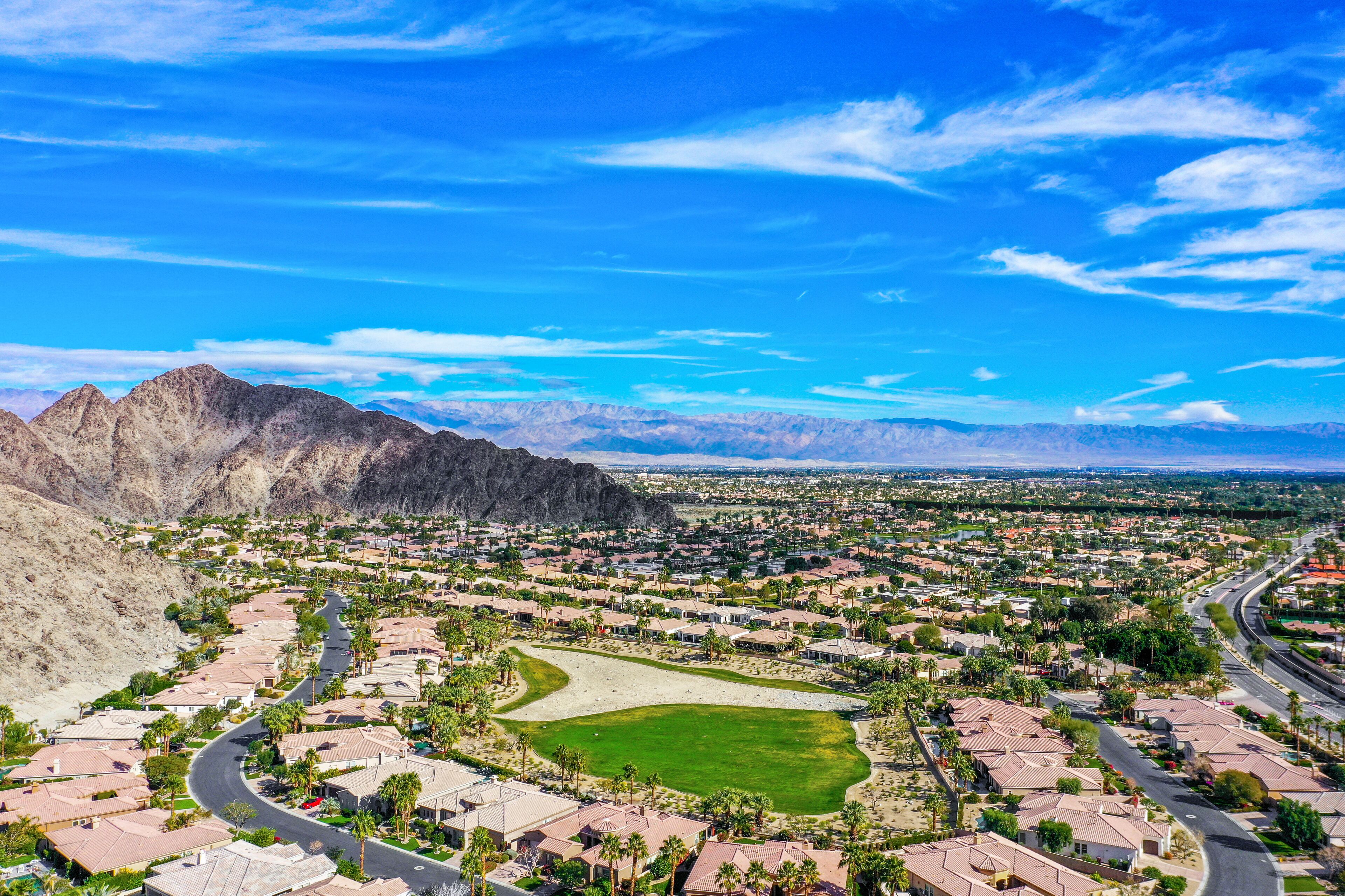 Zona residencial con casas, un campo de golf y montañas al fondo.