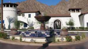 A building with a fountain, surrounded by landscaped gardens and a mountain backdrop. - Have Fun and Relax at Luxury Legacy Villa. Family Friendly or Great for Couples! (La Quinta)