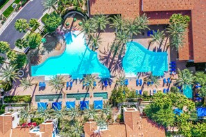An aerial view of a resort with a large swimming pool, palm trees, and sun loungers.