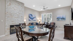 A dining area with a stone fireplace, a round table, and chairs. There is a sofa and a television in the background. - Have Fun and Relax at Luxury Legacy Villa. Family Friendly or Great for Couples! (La Quinta)