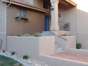A two-story building with a brick facade, a blue door, and a small garden area with rocks and plants. - Fun Under The Sun, Condo 5: This condo is your SUITE RETREAT! (St. George)