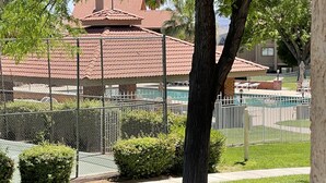 Et afgrænset udendørs område med en pool, et træ og en bygning med rødt tag i baggrunden.