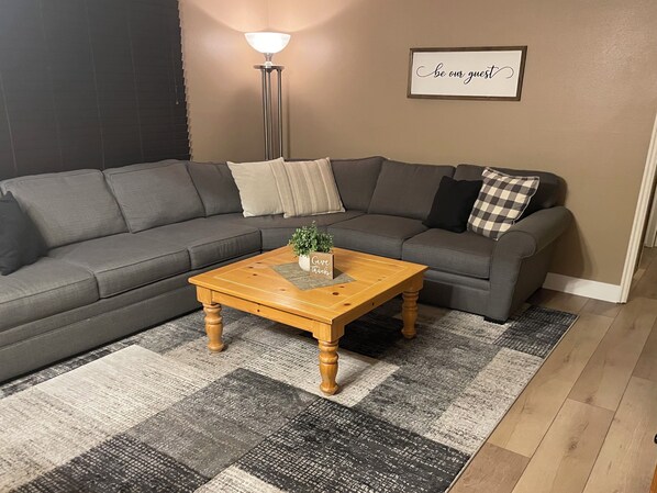 A modern living room with a grey sectional sofa, a wooden coffee table, and a patterned rug.