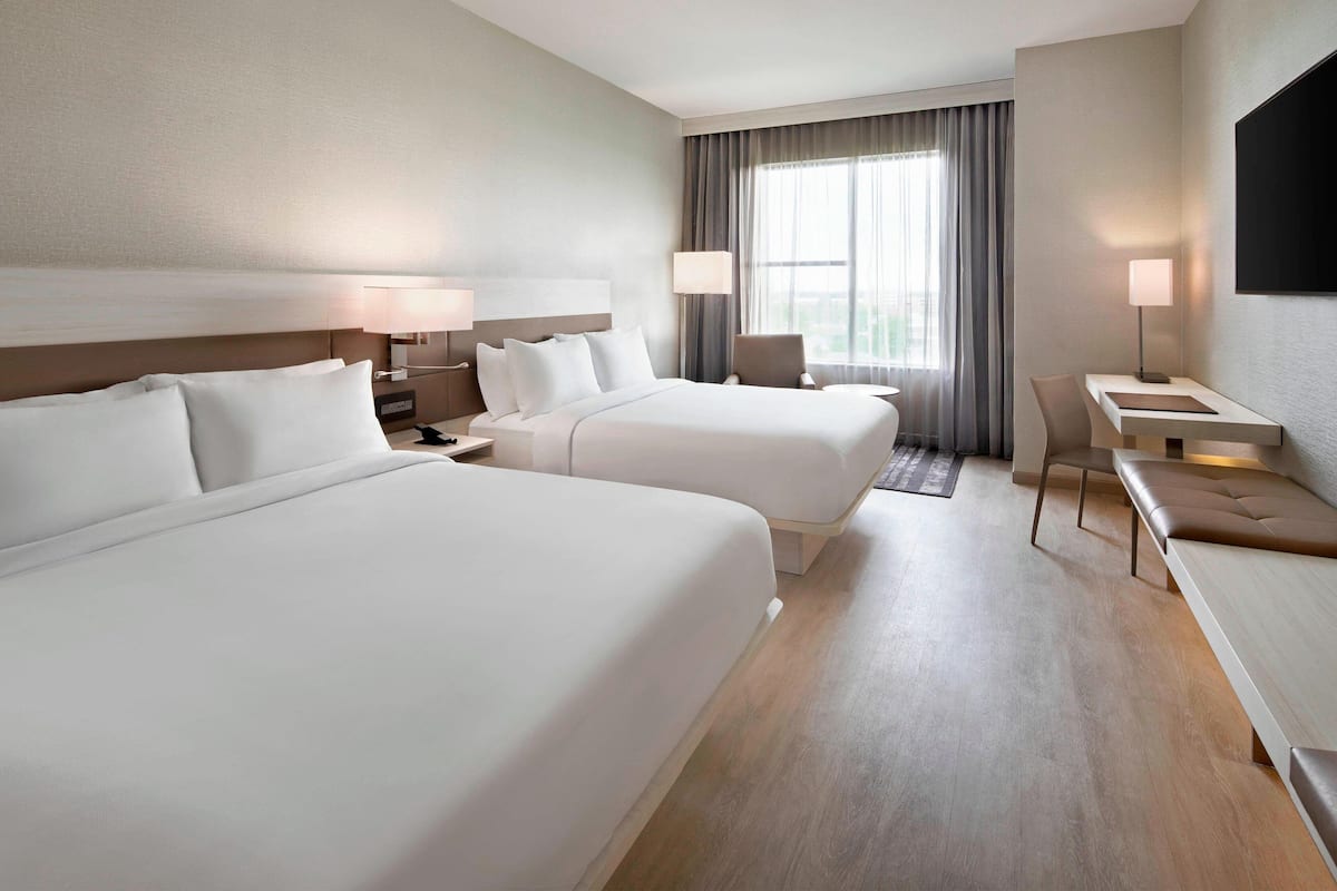 Ein Hotelzimmer mit zwei Betten, einem Schreibtisch, einem Stuhl und einem Fernseher an der Wand.