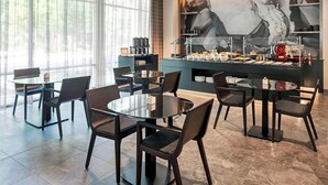 Ein zeitgemäßer Essbereich mit runden Tischen und Stühlen, eine Kaffeebar mit verschiedenen Angeboten und ein großes, abstraktes Gemälde an der Wand.