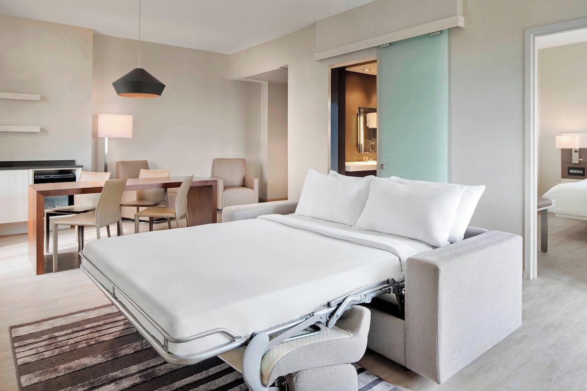 Ein modernes Hotelzimmer mit einer Schlafsofa, einem Essbereich mit Tisch und Stühlen sowie einem separaten Badezimmer.