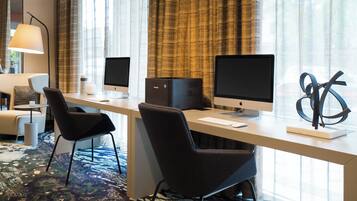 A hotel room with a desk, two chairs, a computer, and a lamp.