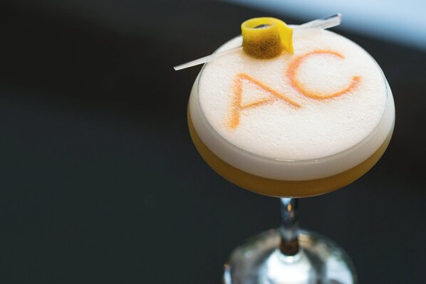 A cocktail with a frothy top and a yellow garnish, served in a stemmed glass.