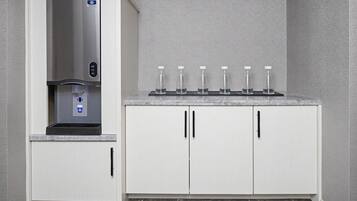 Cozinha com dispensador de água embutido, bancada com seis garrafas de vidro e armários brancos com puxadores pretos.