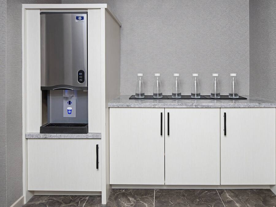 Cozinha com dispensador de água embutido, bancada com seis garrafas de vidro e armários brancos com puxadores pretos.