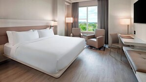 Ein Hotelzimmer mit einem großen Bett, einem Schreibtisch, zwei Stühlen, einem Fernseher und Blick auf Grün.
