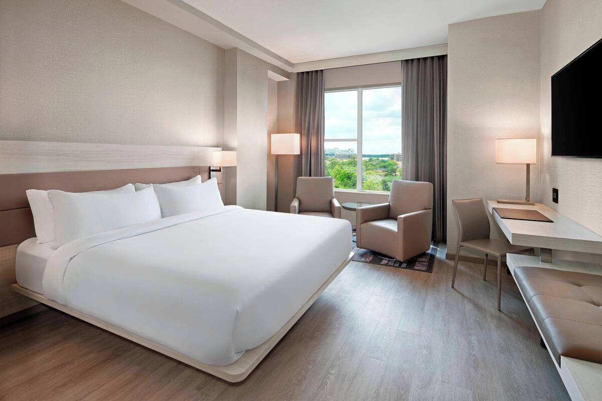 Ein Hotelzimmer mit einem großen Bett, einem Schreibtisch, zwei Stühlen, einem Fernseher und Blick auf Grün.