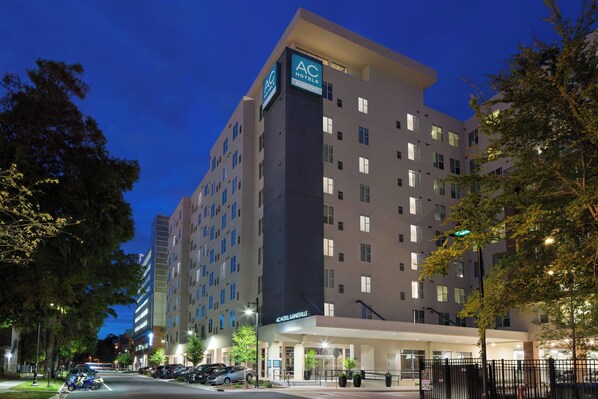 Un hotel de varios pisos con el logotipo AC bien visible, un diseño arquitectónico moderno y una entrada bien iluminada.