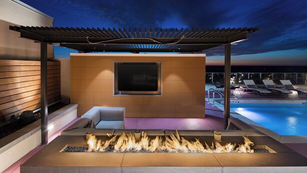 Ein moderner Außenbereich mit Lounge-Möbeln, einem Feuerkorb und Blick auf einen Pool.