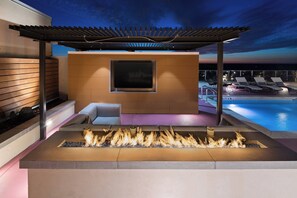 Un espace de détente extérieur moderne, doté d’un foyer, de sièges et offrant une vue sur une piscine.