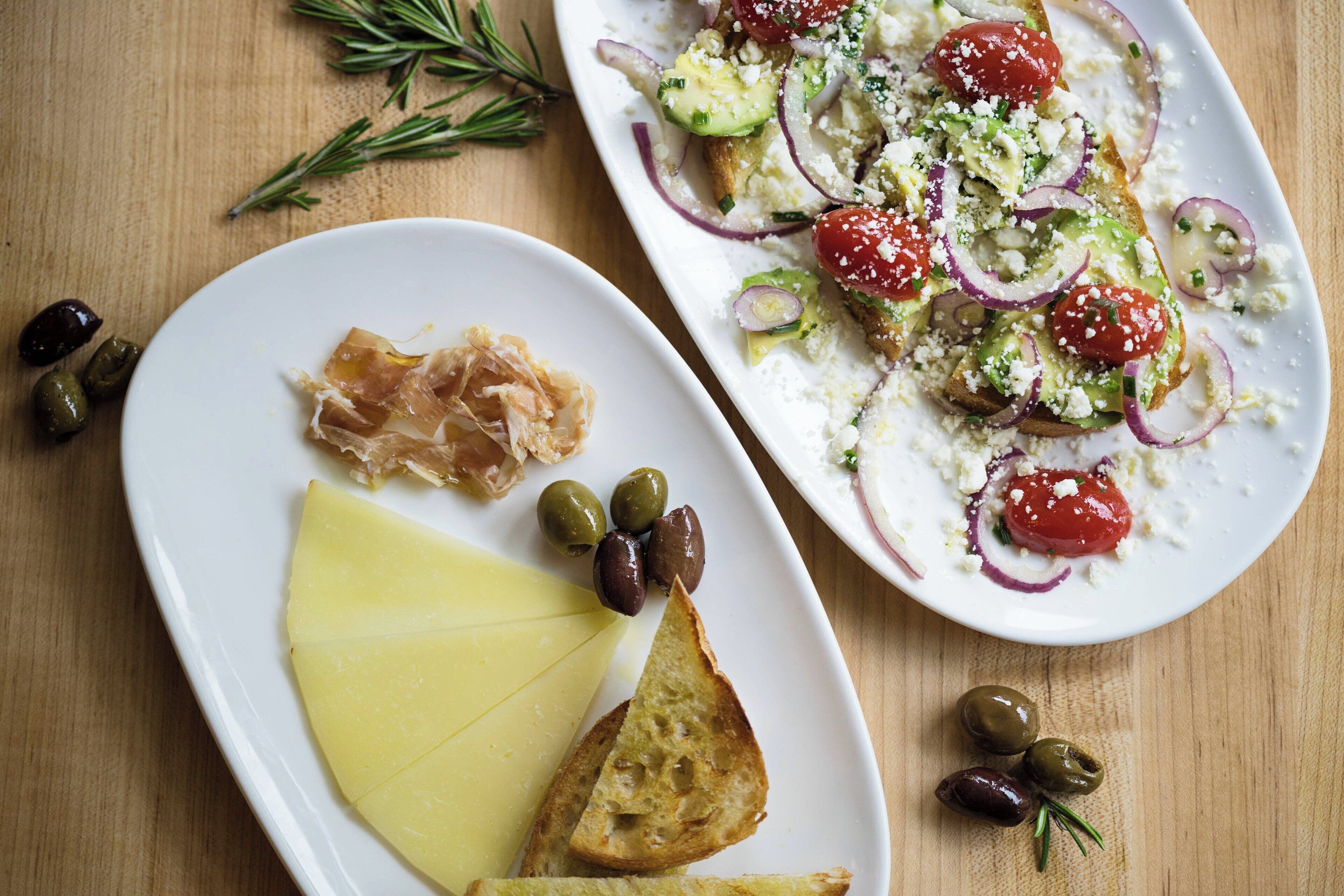 Two plates of food with olives, cheese, and tomatoes on a wooden table.