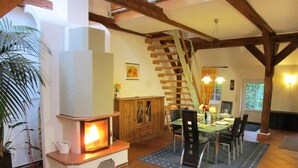 A cozy living room with a fireplace, wooden beams, a dining area, and a staircase. - Spacious vacation residence for 6 pers. with pool and garden. Sauna - shared use (Stadland-Reitland)