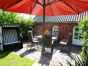 A patio area with a brick wall, a red umbrella, and outdoor furniture including a striped bench and chairs.