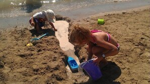 Une plage de sable où deux personnes creusent des trous dans le sable : l’une tient une pelle et l’autre un seau.
