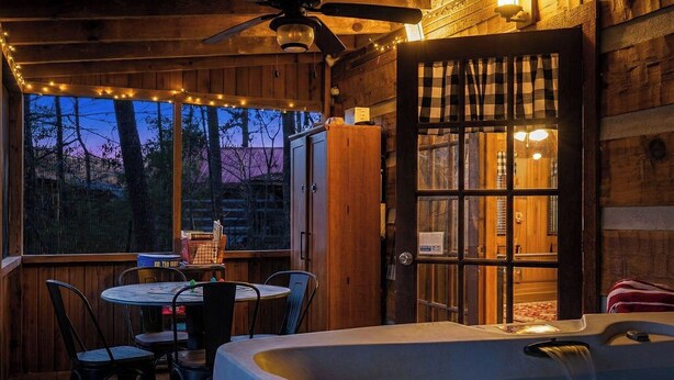 Una cabaña de madera con un jacuzzi, un comedor con sillas, una mesa y un ventanal con vistas a los árboles.