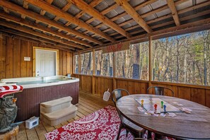 Une terrasse en bois avec un jacuzzi, une table avec des jeux de cartes et une vue sur la forêt.