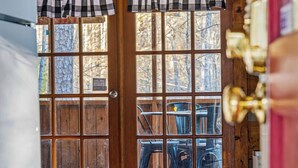 Interior de madera con una puerta doble, un ventilador de techo y vistas a muebles de exterior a través de la puerta.