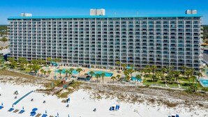 A large hotel with multiple floors, a swimming pool, and a beach area with sun loungers. - Gulf-Front Comfort, Personally Prepared for You (Panama City Beach)