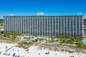 Un grand hôtel à plusieurs étages, doté d’une piscine et d’un espace de plage avec des chaises longues.