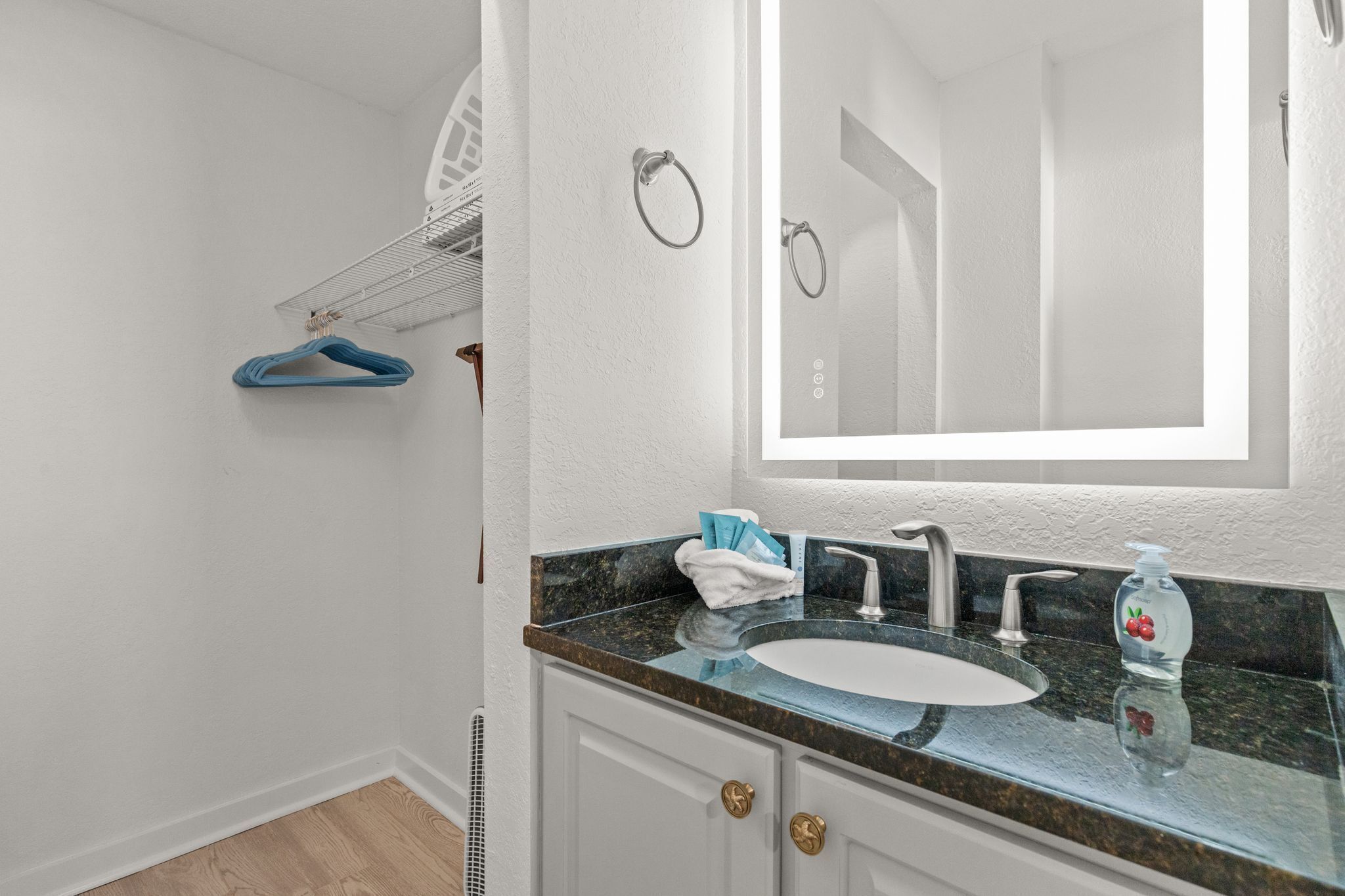 Un baño con lavamanos blanco, espejo, toallero y dispensador de jabón.