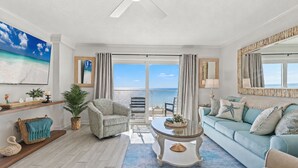 Un salon avec vue sur l’océan, un ventilateur de plafond et une grande fenêtre.