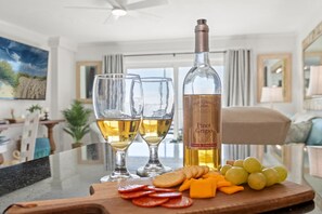 A bar area with two glasses of white wine, a bottle of Pinot Grigio, and a variety of snacks on a wooden board.