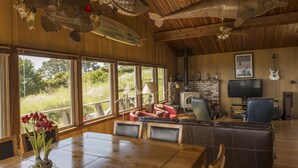 A spacious living area with a large wooden ceiling, a stone fireplace, a television, and a guitar. - Pelican Point, Dramatic Ocean & Coast Views, Spa, Next to Town (Mendocino)