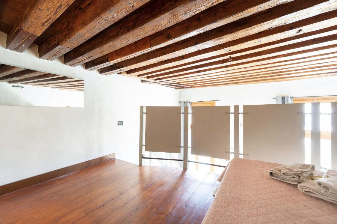 A room with wooden beams, a bed with towels, and a window.