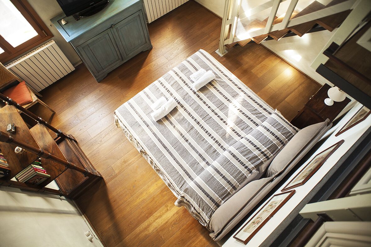 A bedroom with a wooden floor, a striped bedspread, and a television on a cabinet.