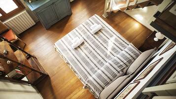 A bedroom with a wooden floor, a striped bedspread, and a television on a cabinet.