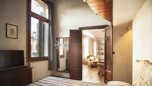 Ein Schlafzimmer mit einem Bett, einem Fernseher, einem Fenster und einer Tür zu einem weiteren Raum.