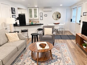 Een moderne woonkamer met een grijze bank, een ronde salontafel en een eethoek met een witte tafel en stoelen.