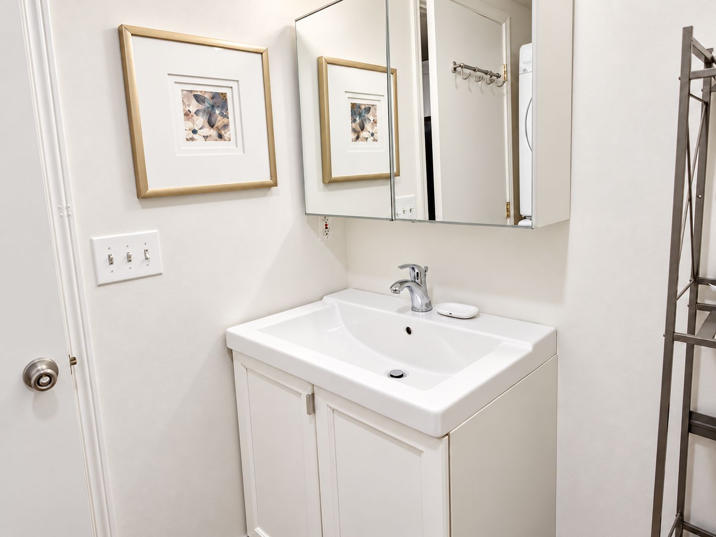 Une salle de bain avec un lavabo blanc, un miroir et des œuvres d’art encadrées accrochées au mur.
