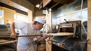 A person in a white uniform operating a large industrial oven, likely for baking or cooking, in a commercial kitchen setting.