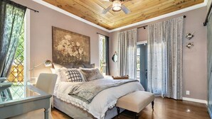 A bedroom with a bed, a desk, a ceiling fan, and a large window with curtains.