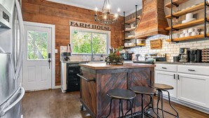 A kitchen with a farmhouse theme, featuring wooden walls, a central island with stools, and a sign that reads "FARM HOUSE".