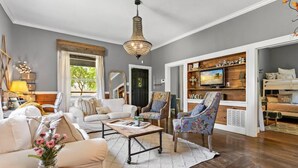A spacious living room with a large window, a chandelier, a television, and a cozy seating area.