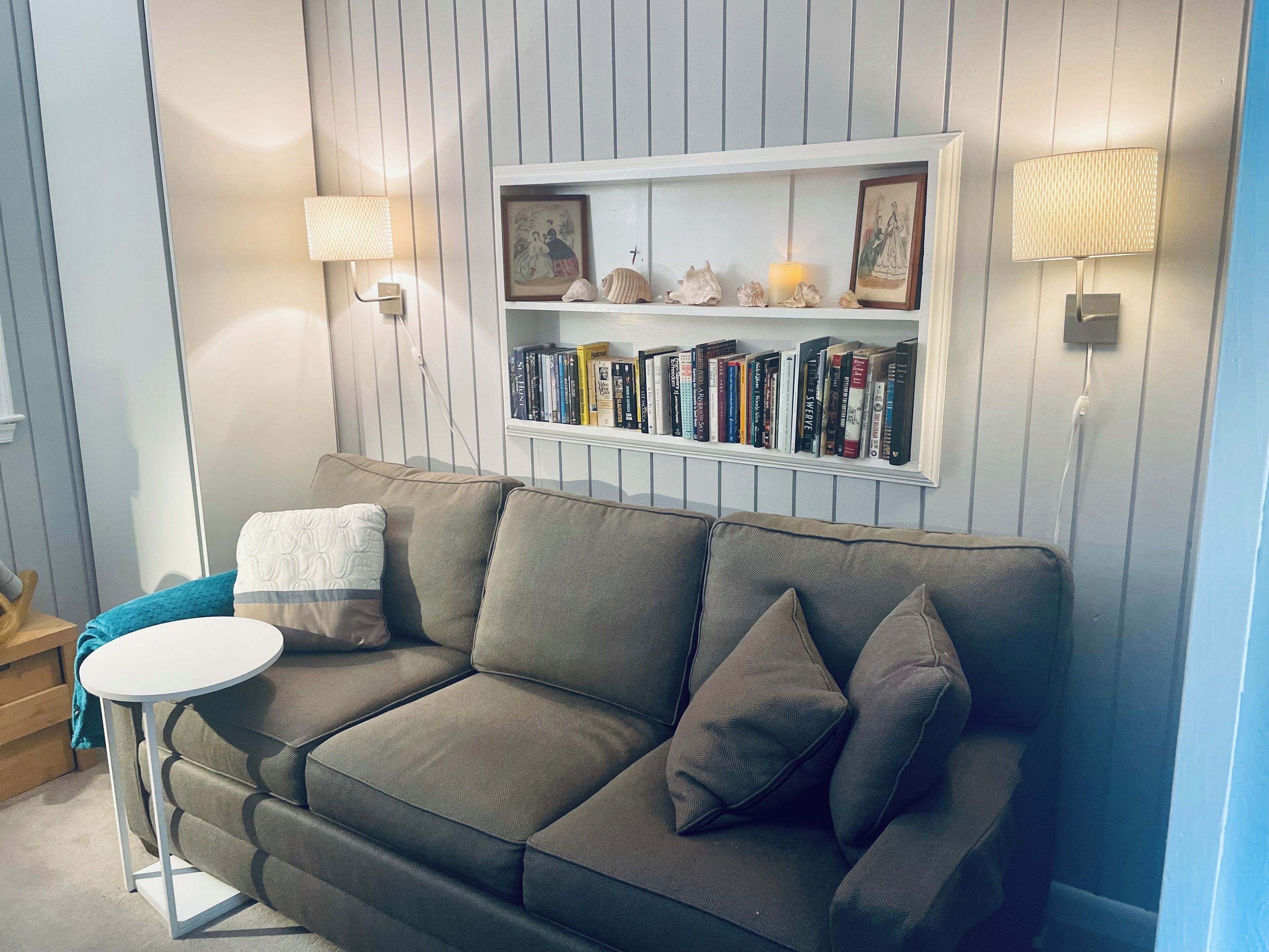 A modern living room with a grey sofa, a small round table, and a bookshelf with books and decorative items.