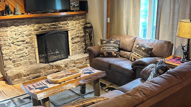 A cozy living room with a stone fireplace, leather sofa, and a flat-screen TV mounted above the fireplace.